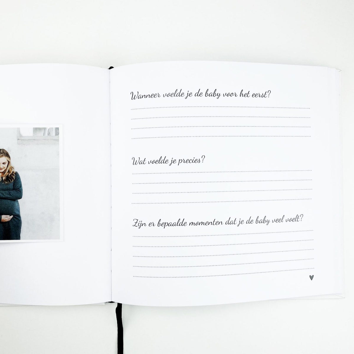 Open zwangerschapsdagboek met vragen over de eerste babybewegingen, een zwangerschapsfoto en zwart leeslint.