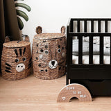 Houten regenboogletterbord met 'born to be wild' op de vloer naast een zwart babybed en twee dierenmanden.