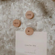 Drie ronde eikenhouten Hello Love-magneten met ‘Hello’, ‘Love’ en een hartje, waarvan één een kaart vasthoudt.