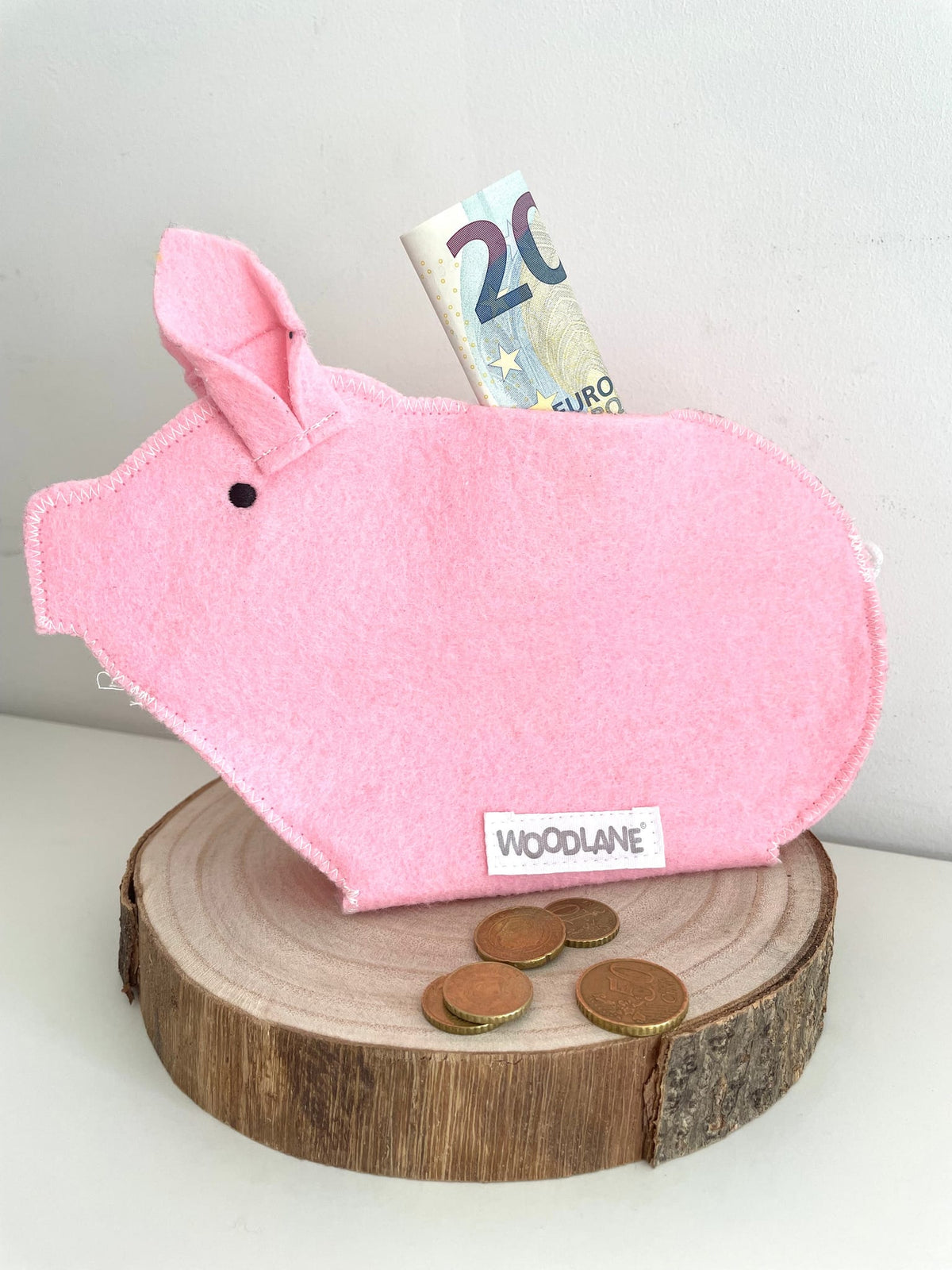 Roze Piggy-spaarvarken met een biljet van 20 euro en munten op een houten schijf