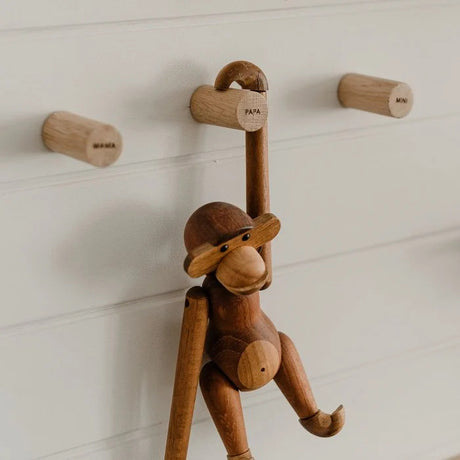 Drie houten Family-wandhaken aan een witte wand, met een houten aap aan de haak met opschrift Papa.